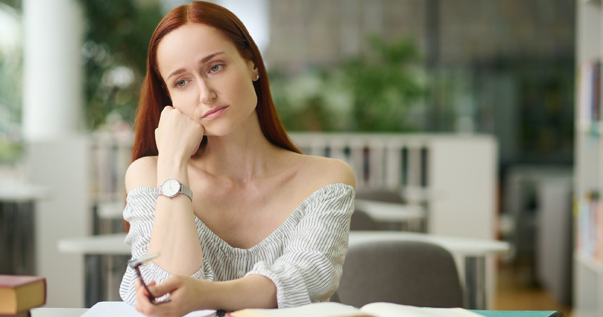 Sad woman sitting at table with books